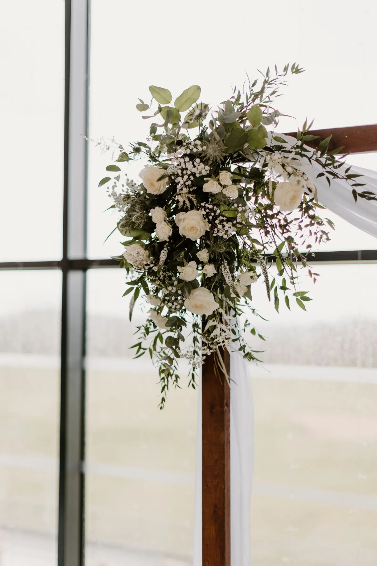 White roses and eucalyptus at the corner of an arch, in soft window light