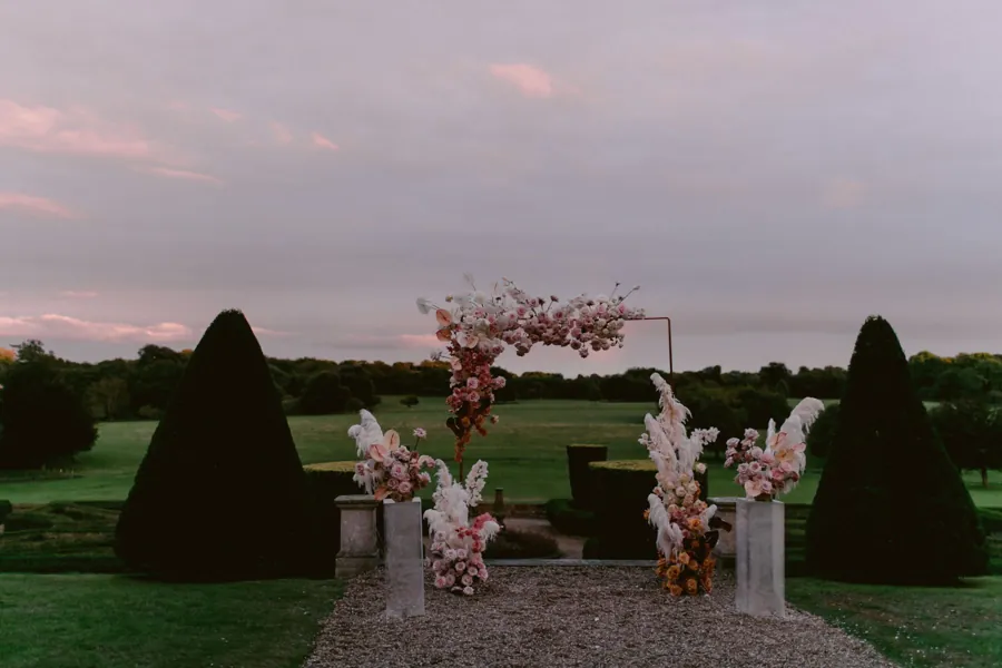 An arch with blush and mauve florals at dusk on a gravel terrace