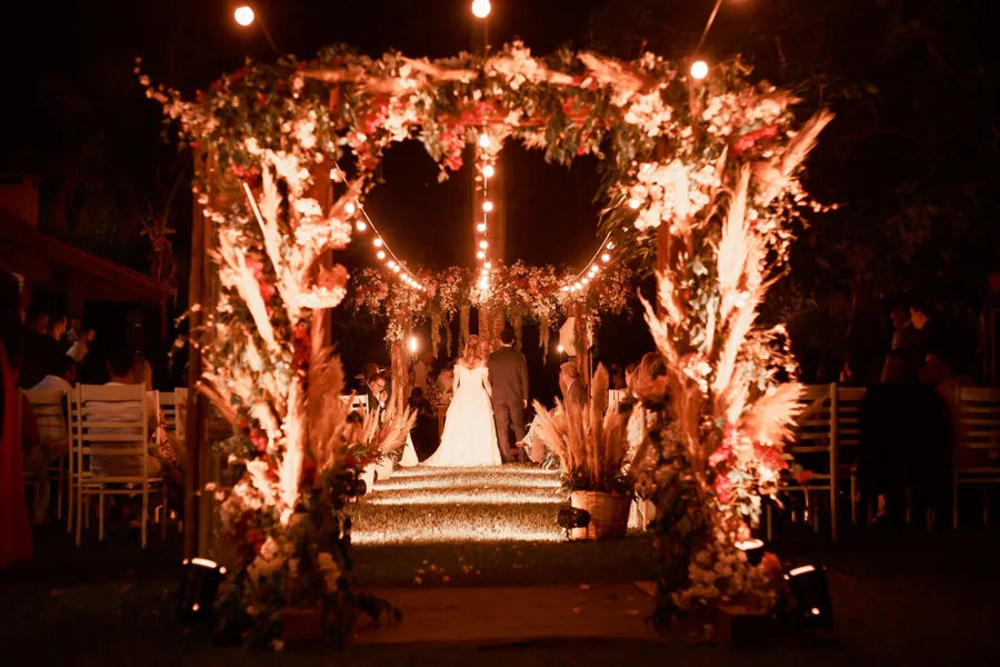 A floral arch lit warmly at night with a couple beneath it